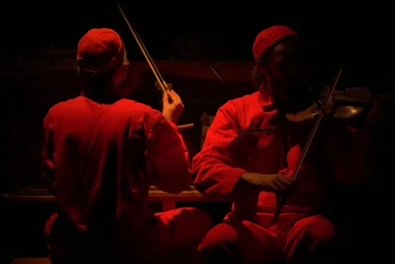 Photo de deux comédiens habillés en rouge jouant du violon