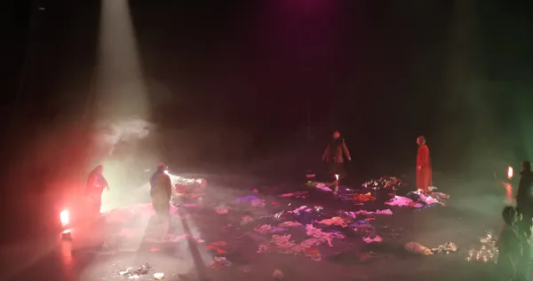 Photo de la scène vue du dessus, avec plusieurs comédiens et des lumières entre rose et rouge