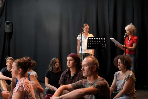 Photo de deux comédiennes en train de lire, et d'un groupe de personnes assises devant elles