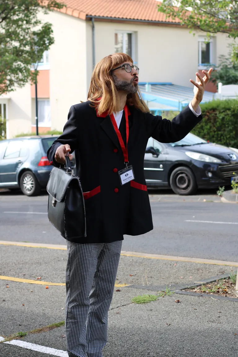 Photo d'un comédien, une mallette à la main, expliquant quelque chose dans la rue. 