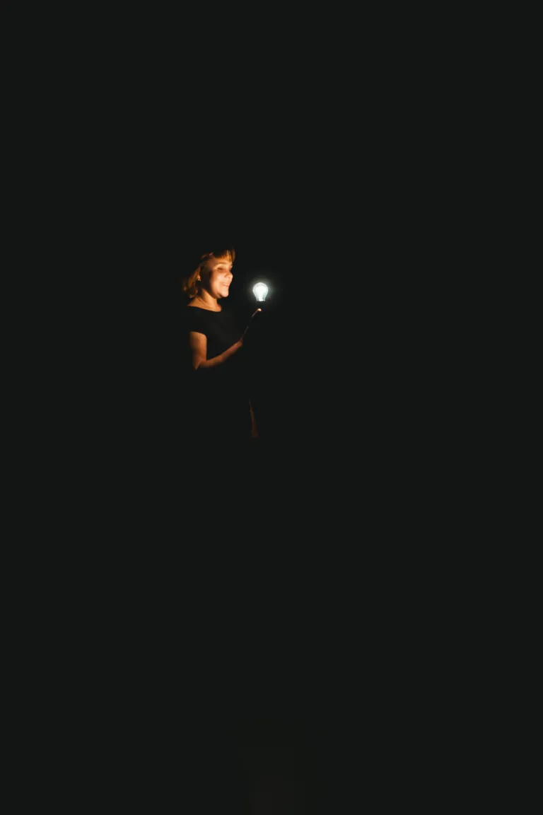 Photo d'une comédienne dans le noir avec une ampoule allumée devant le visage