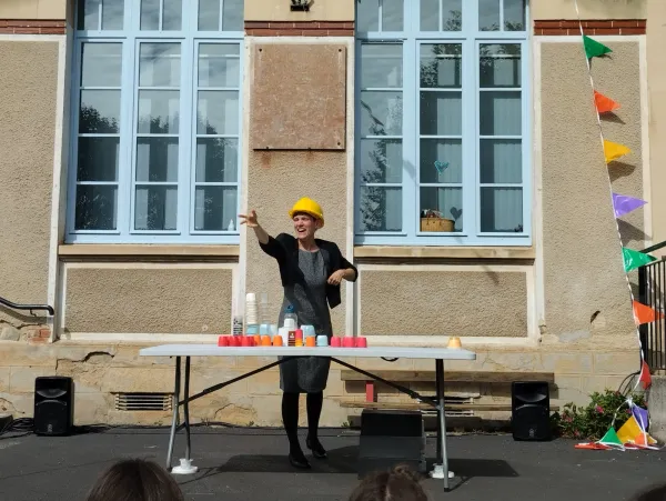 Photo d'une comédinne en extérieur, derrière une table et avec un casque de chantier