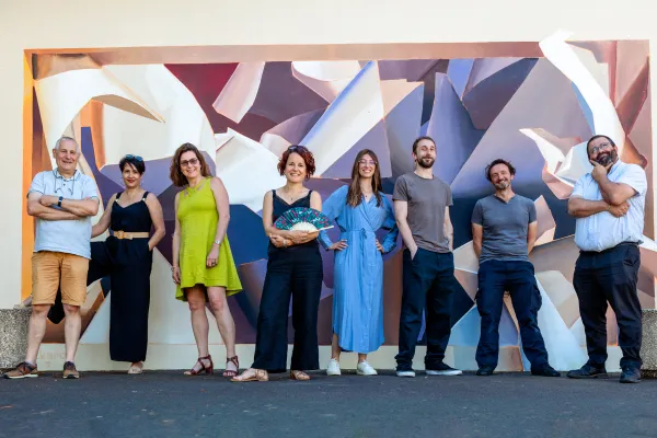 Photo des 8 agents permanents de la Cour des 3 Coquins devant la fresque à l'intérieur de la Cour. 